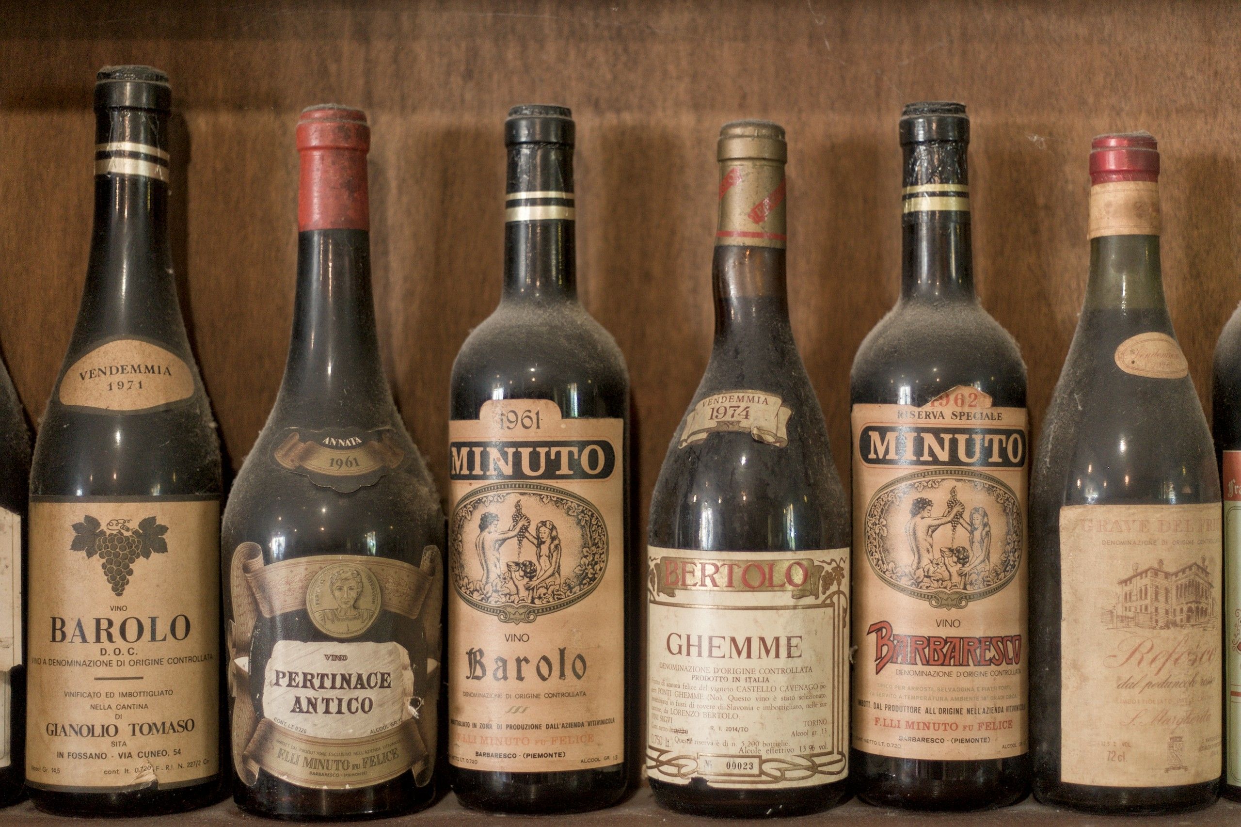 Vecchie bottiglie di Barolo, Barbaresco e Ghemme degli anni Sessanta e Settanta, impolverate, su uno scaffale di legno