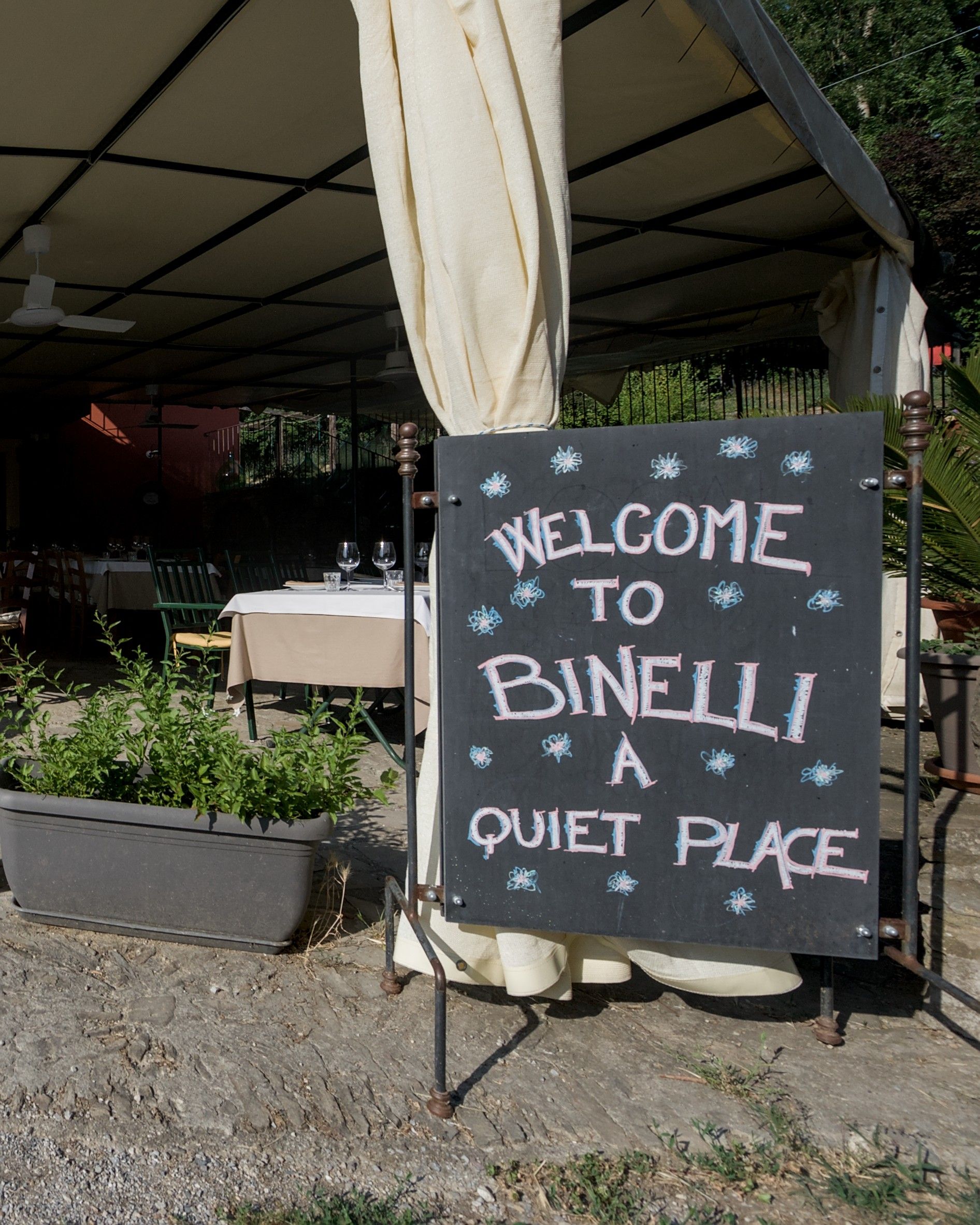 La lavagna all'ingresso della terrazza con la scritta «Welcome to Binelli, a quiet place», con i tavoli apparecchiati sullo sfondo