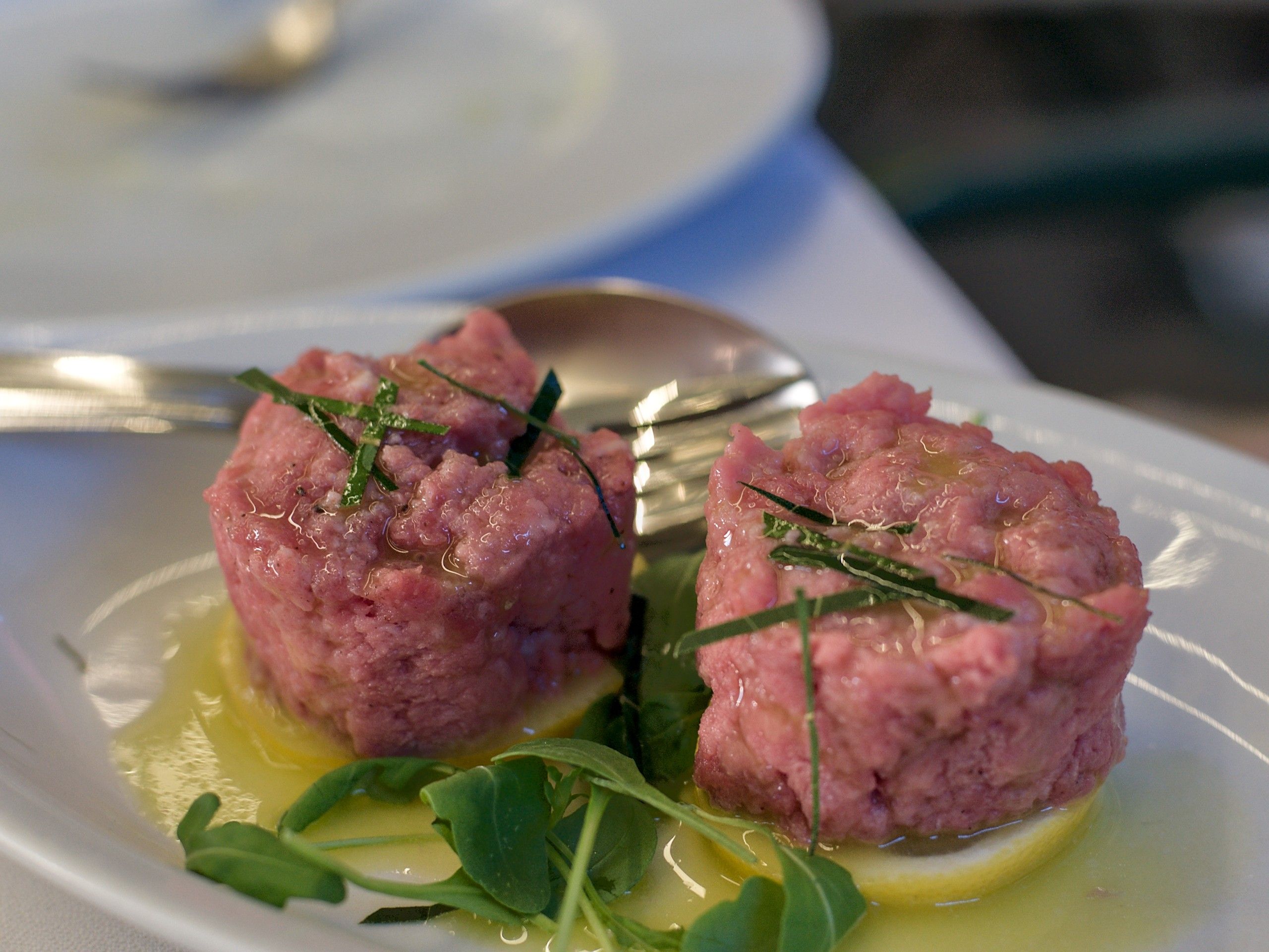 Due porzioni di carne cruda battuta al coltello, con olio, limone e rucola, su un piatto bianco