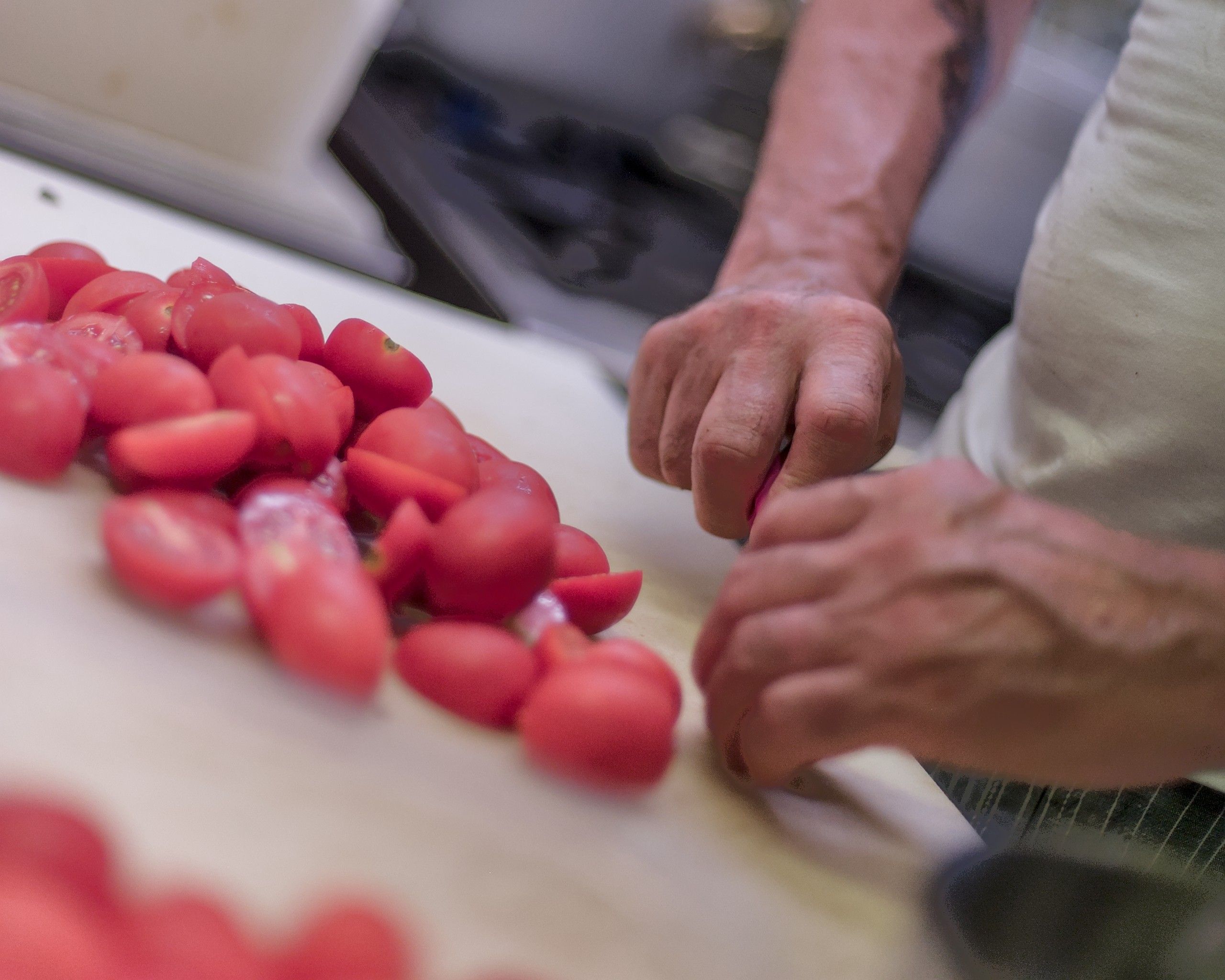 Le mani di Fabio che tagliano pomodorini freschi sul tagliere, in cucina