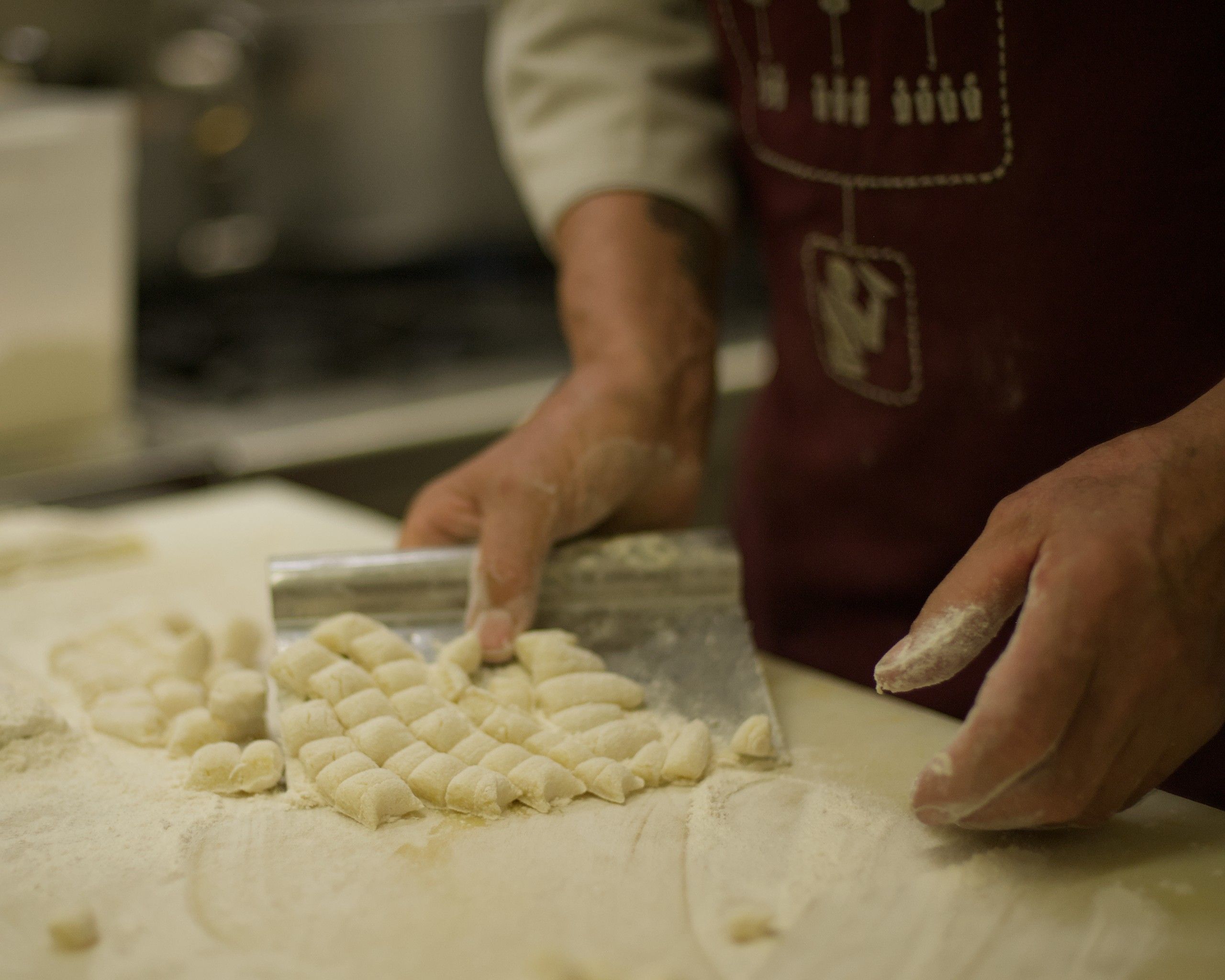 Le mani di Fabio che raccolgono con la spatola gli gnocchi appena tagliati, sul tagliere infarinato