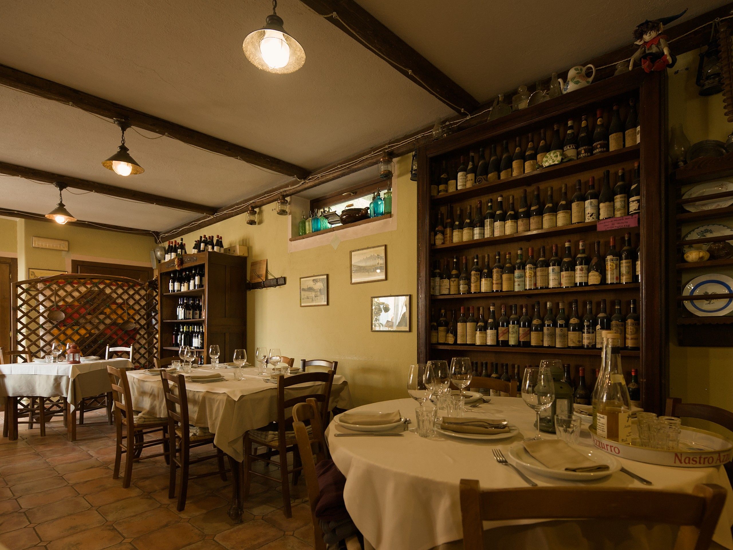 La sala interna con i tavoli apparecchiati, le lampade accese e gli scaffali dei vini